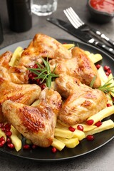 Delicious grilled chicken wings with french fries served on grey table, closeup