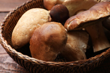 Fresh porcini mushrooms in wicker basket on wooden table, closeup