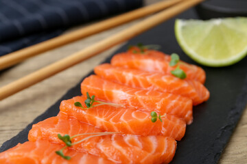 Fresh salmon sashimi with microgreens and lime on wooden table, closeup