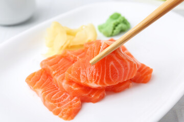 Taking fresh salmon sashimi with chopsticks from plate at light table, closeup
