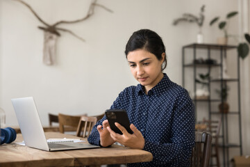 Millennial woman texting on phone during work session on laptop