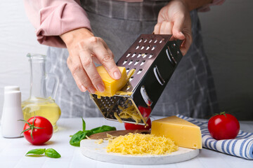 Woman grating cheese at white tiled table, closeup