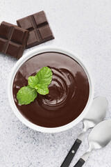 Melted chocolate with mint in bowl, pieces and spoons on light grey table, flat lay