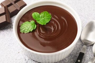 Melted chocolate with mint in bowl, pieces and spoon on light grey table, closeup