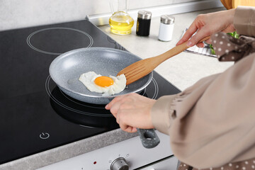 Woman taking fried egg with slotted spatula in kitchen, closeup
