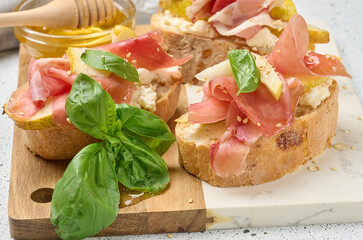 Italian bruschetta with prosciutto, pear, soft cheese, honey and sesame seeds. The dish is served on a light marble board