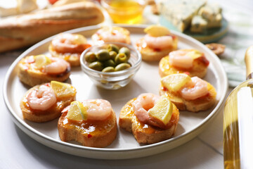 Tasty bruschettas with shrimps, lemon, sauce, olives and wine on white wooden table, closeup