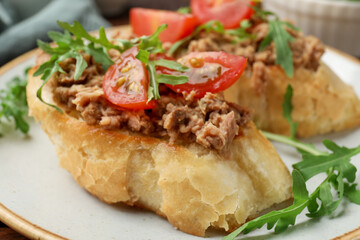 Delicious bruschettas with tuna, tomatoes and arugula on plate, closeup