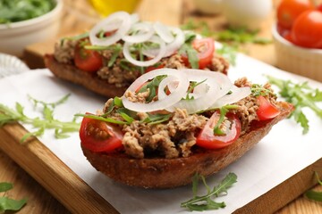 Delicious bruschettas with tuna, tomatoes, onion and arugula on wooden table, closeup