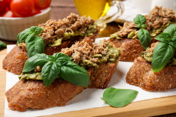 Delicious bruschettas with tuna, avocado and basil on table, closeup