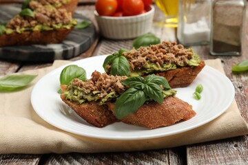Delicious bruschettas with tuna, avocado and basil on wooden table, closeup