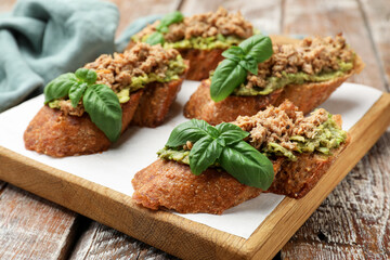 Delicious bruschettas with tuna, avocado and basil on wooden table, closeup