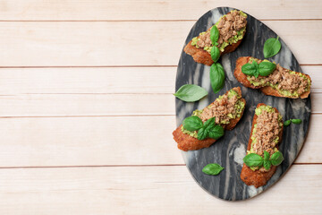 Delicious bruschettas with tuna, avocado and basil on light wooden table, top view. Space for text