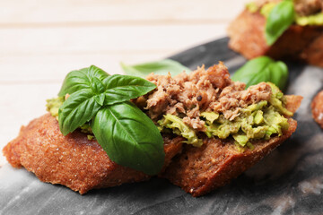Delicious bruschettas with tuna, avocado and basil on table, closeup