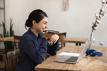 Smiling woman record audio notes on smartphone working on notebook