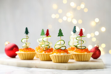 Christmas food. Tasty tartlets with red caviar, cream cheese, cucumber and decor on white marble...