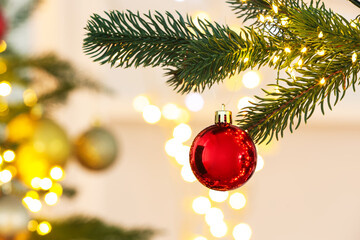 Christmas bauble hanging on fir tree branch against blurred festive lights, closeup. Bokeh effect