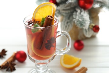 Tasty punch drink in glass, spices and Christmas decor on white wooden table, closeup. Space for text