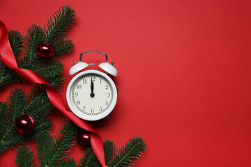 Alarm clock, fir tree branches, ribbon and baubles on red background, flat lay with space for text....