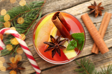 Tasty punch drink in glass, spices and Christmas decor on wooden table, flat lay. Bokeh effect