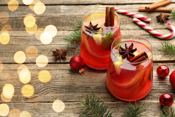 Tasty punch drink in glasses, spices and Christmas decor on wooden table, space for text. Bokeh effect