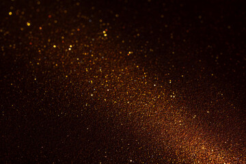 Dark brown textured surface illuminated from bottom right, light accentuates micro relief and makes golden glitter fragments sparkle vividly against shadowed background