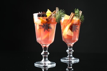 Tasty punch drink with spices in glasses on mirror surface against black background, closeup