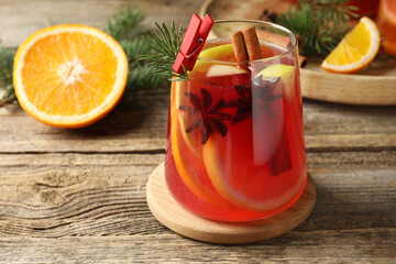 Tasty punch drink in glass, spices, orange and Christmas decor on wooden table, closeup