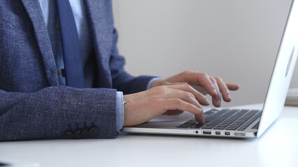 Close up of businessman's hands typing on laptop keyboard, working diligently in a modern office...