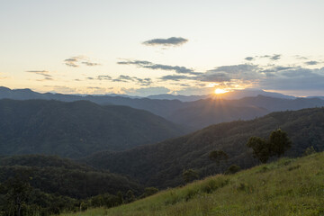 Obraz premium Serene mountain landscape at sunset with beautiful, peaceful view over green valley. sun setting behind cloudy sky creates scenic and tranquil moment in nature