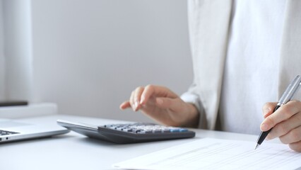 Fototapeta premium Businesswoman is calculating annual tax using calculator and taking notes in the office, managing domestic budget and checking financial documents. Audit and taxes in business