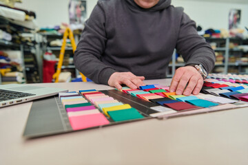 Designer working with fabric swatches, color palette selection for fashion design, textile industry, creative process, laptop, material samples, studio shot.