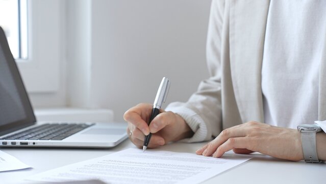 Businesswoman signing a contract at her office desk, surrounded by a laptop and documents, exemplifies focus and commitment. Business people concept