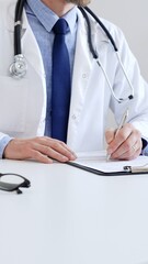 Unreckognisable doctor man writing a prescription and filling out medical records on a clipboard in an office setting. Medicine and health care concept