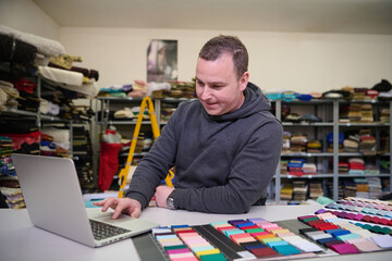 Fashion designer using laptop with fabric swatches in workshop, textile business owner working at his desk, checking inventory, managing online orders, small business owner concept.