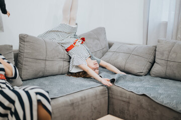 A playful child dressed in a polka dot dress energetically engaging in activities on a couch in a comfortable home setting, illustrating joy, fun, and the warmth of family life.