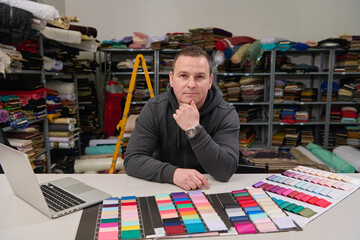 Tailor or designer in his workshop with fabric samples, looking at fabric swatches and laptop, textile industry, small business owner, entrepreneur, fashion design studio.