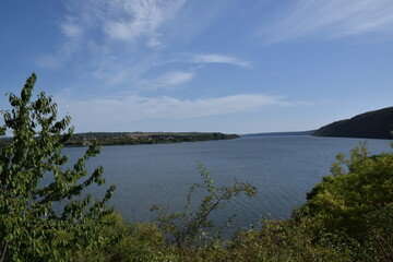 Serene landscape view of a calm river surrounded by lush greenery and distant hills under a clear blue sky, showcasing the beauty of nature and tranquility