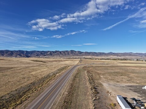 Drone view of scenic Chatfield Colorado highway stretching toward majestic Rocky Mountains under clear blue sky