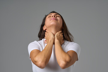 Woman holding neck in pain and looking up showing tension or discomfort in throat area indoors