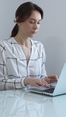 Professional businesswoman working on laptop, sitting at glass desk in bright contemporary workspace, embodying corporate success and concentration. Business people concept.
