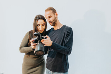 A man and woman collaborate by reviewing camera settings, embodying teamwork and creative interaction in a bright indoor studio setting.