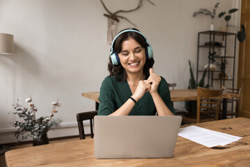 Happy young woman wearing headphones communicate online via notebook