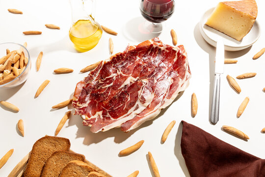 Serrano ham plate with appetizers, mediterranean food on white table.
