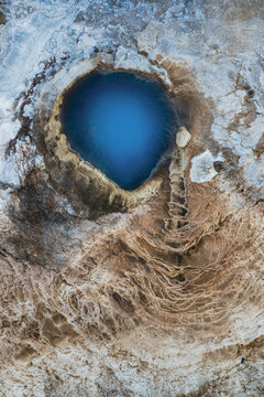 Aerial view of a mesmerizing azure pool nestled within a textured landscape of earthy browns and creams, creating a striking contrast in Iceland's geothermal area, Iceland.