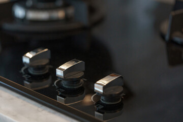Close-up of modern metallic control knobs on a black glass kitchen cooktop.