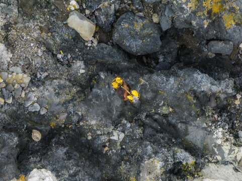 Aerial view of a lone worker amidst the harsh, volcanic landscape, navigating the treacherous terrain of Mount Ijen, East Java, Indonesia.