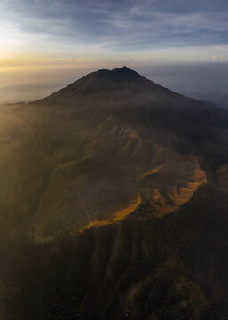 Aerial view of the majestic Mount Ijen shrouded in golden light, casting long shadows across the rugged terrain, East Java, Indonesia.