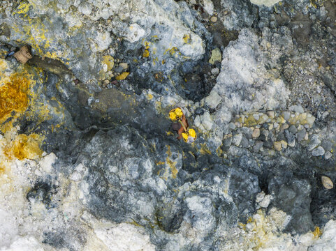 Aerial view of mineral deposits swirling with bright yellow sulfur against a backdrop of grey and white rocks, creating a mesmerizing natural canvas, Mount Ijen, East Java, Indonesia.