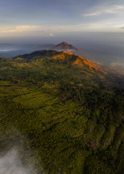 Aerial view of a rugged landscape where golden light kisses the peaks of mountains amidst a sea of green vegetation, Mount Ijen, East Java, Indonesia.